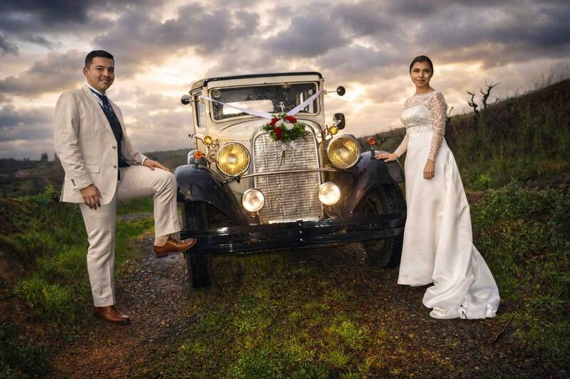 Sesión fotográfica de novios junto a automóvil vintage en un entorno natural durante matrimonio.